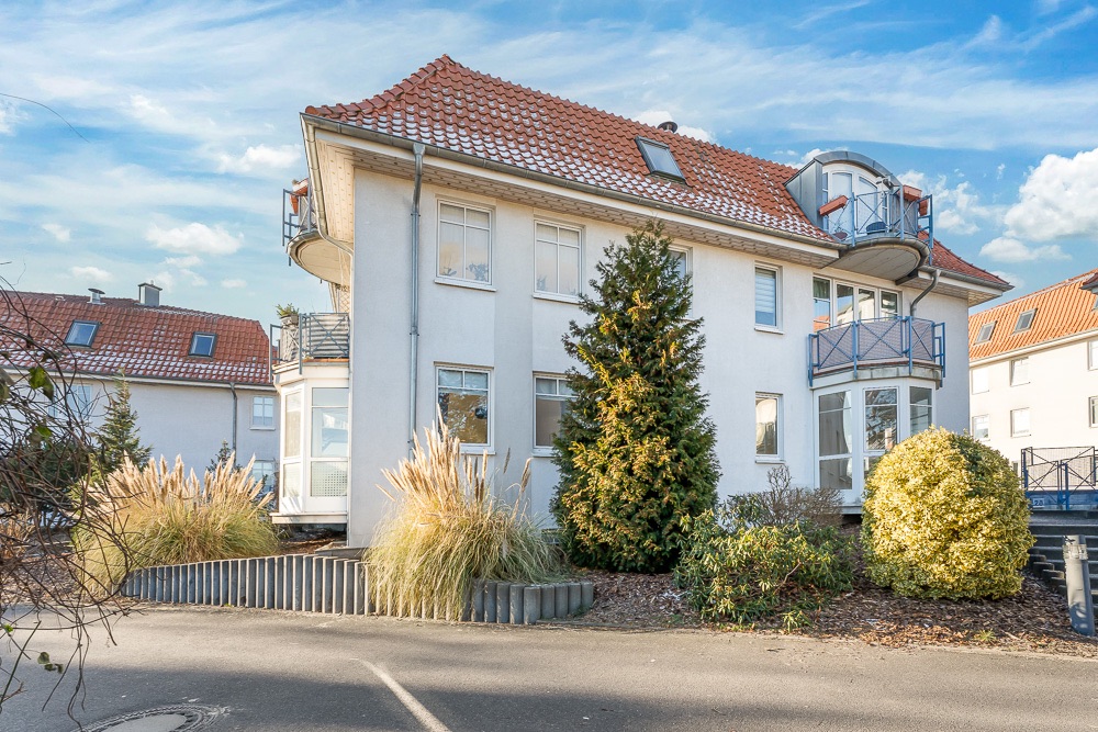 Modernes Wohnhaus mit rotem Ziegeldach, Balkonen und gepflegten Sträuchern im Vorgarten.