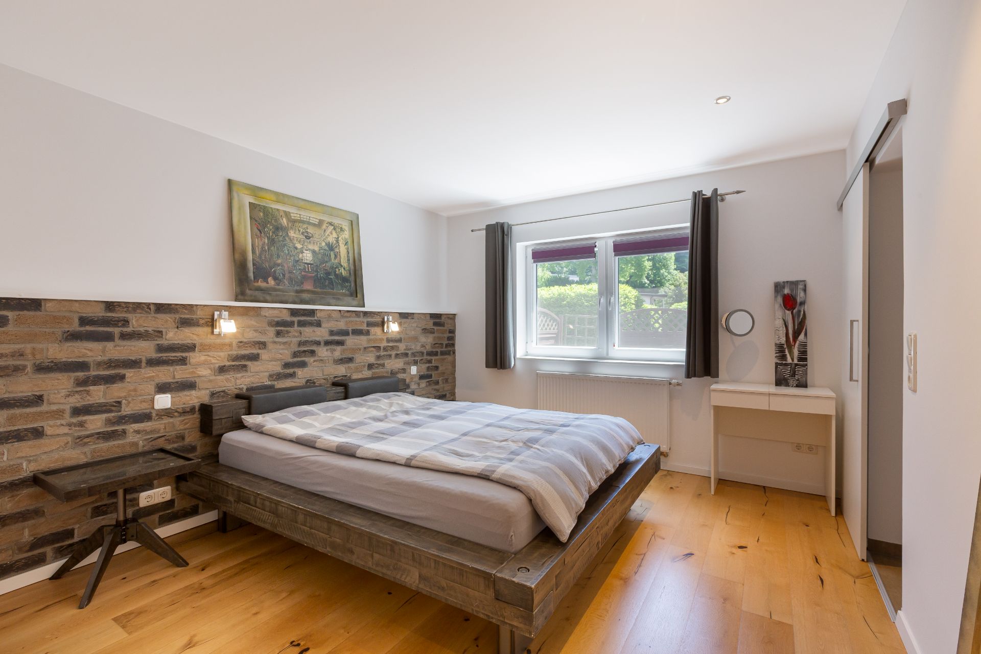 Helles Schlafzimmer mit Holzboden, Doppelbett, gemusterten Wänden und Fenster mit blickdichten Vorhängen.
