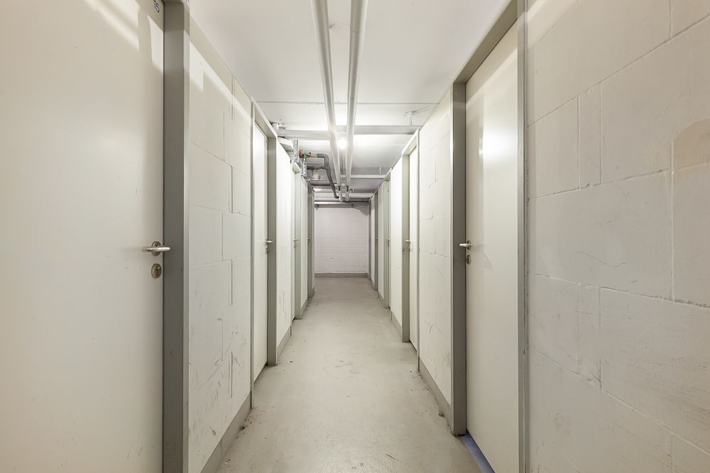 Heller Flur mit mehreren weißen Türen und sichtbaren Rohrleitungen an der Decke.