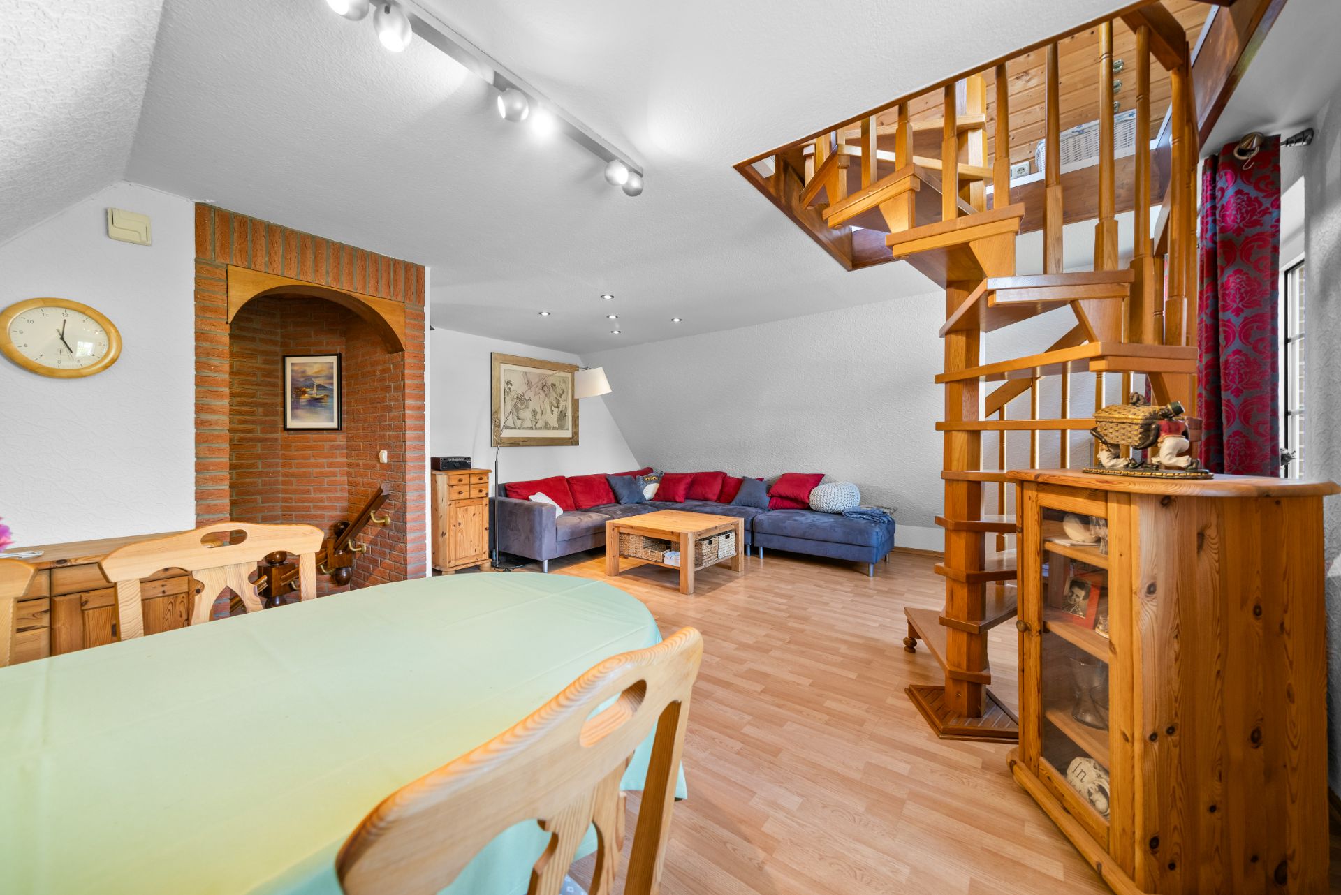 Wohnzimmer mit Holztreppe, Sofa, Couchtisch und Essbereich mit Holzmöbeln.