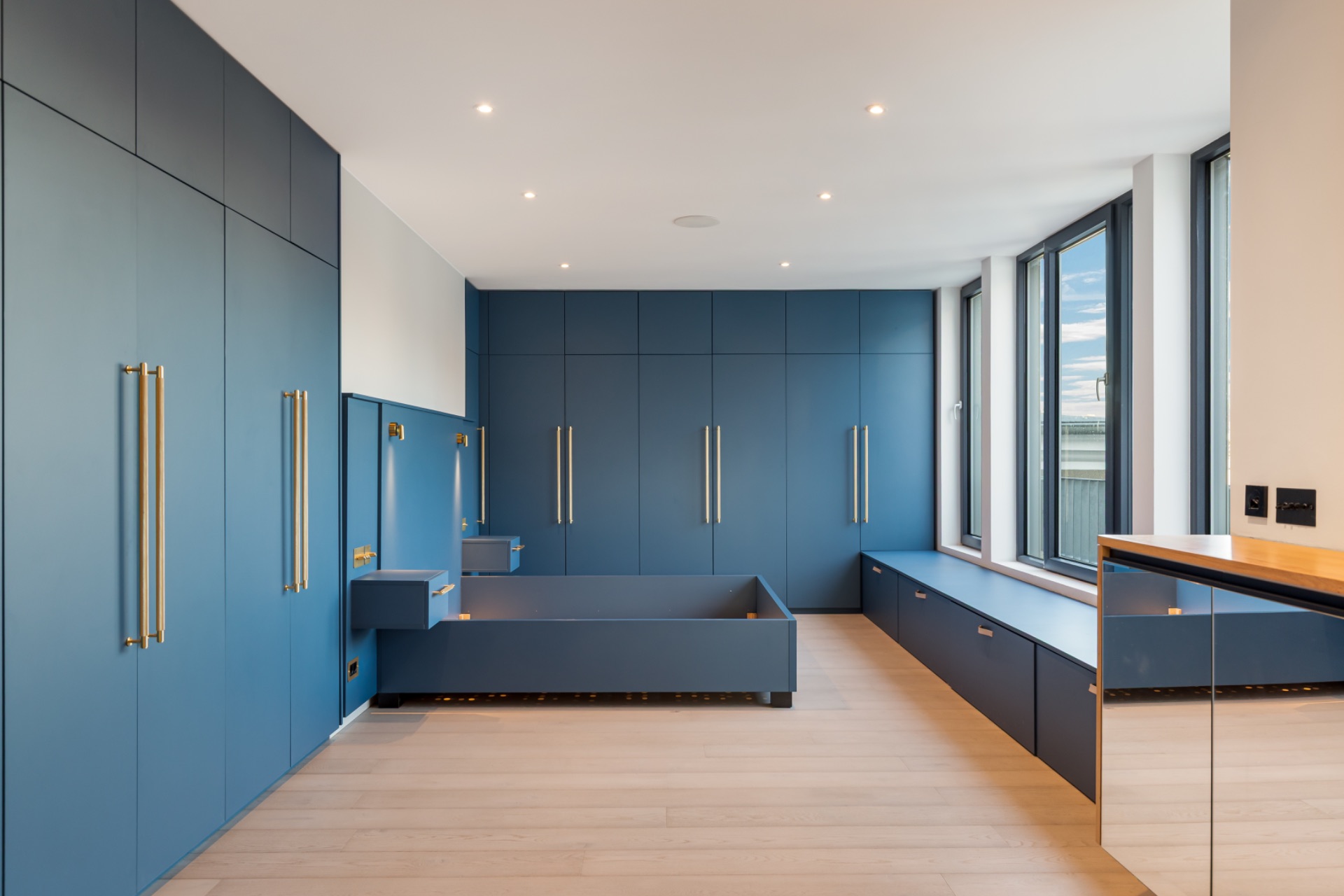 Modernes Schlafzimmer mit blauen Einbauschränken, großem Bettgestell und breiten Fenstern.