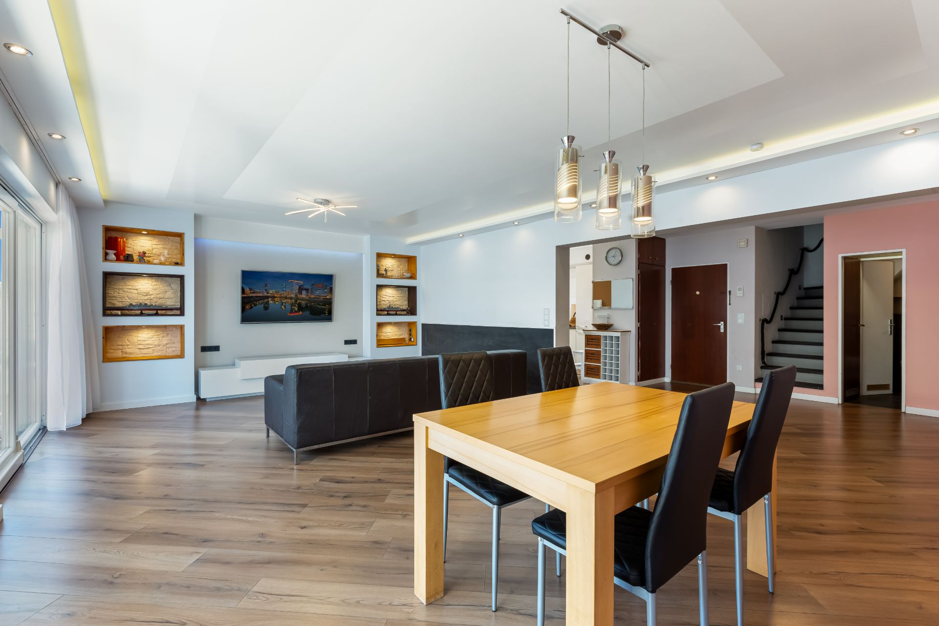 Modernes Wohn- und Esszimmer mit Holzboden, Esstisch, Sofa, Fernseher und Regalen an der Wand.