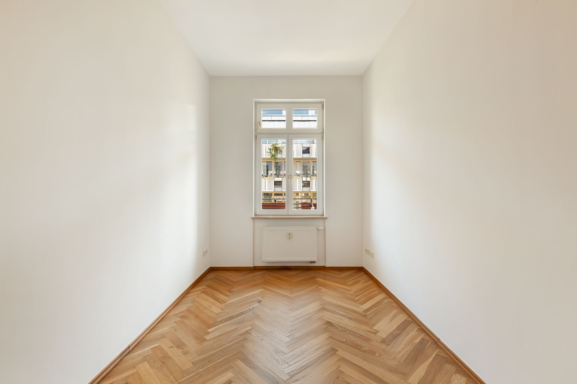 Leerer, heller Raum mit Parkettboden und einem Fenster in der Mitte der Stirnwand.