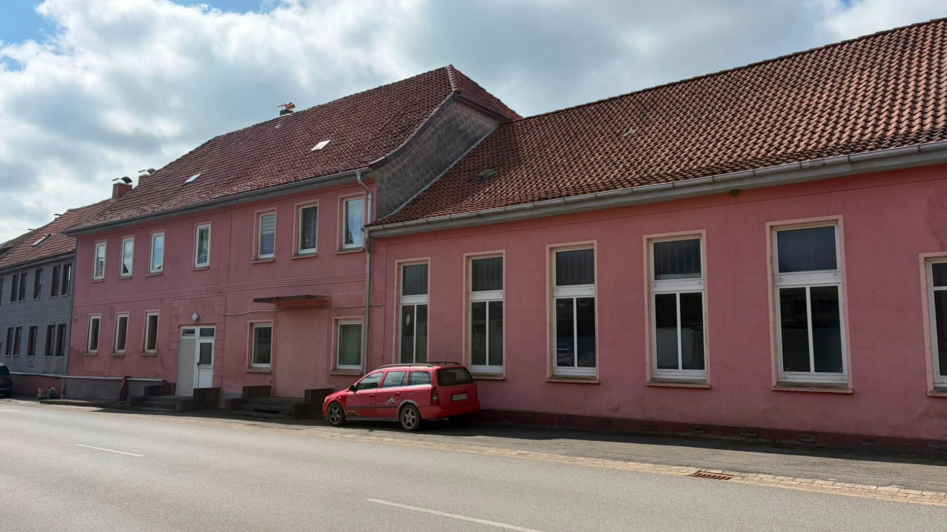 Pinkes Wohngebäude mit vielen Fenstern und einem roten Auto davor an einer Straße.