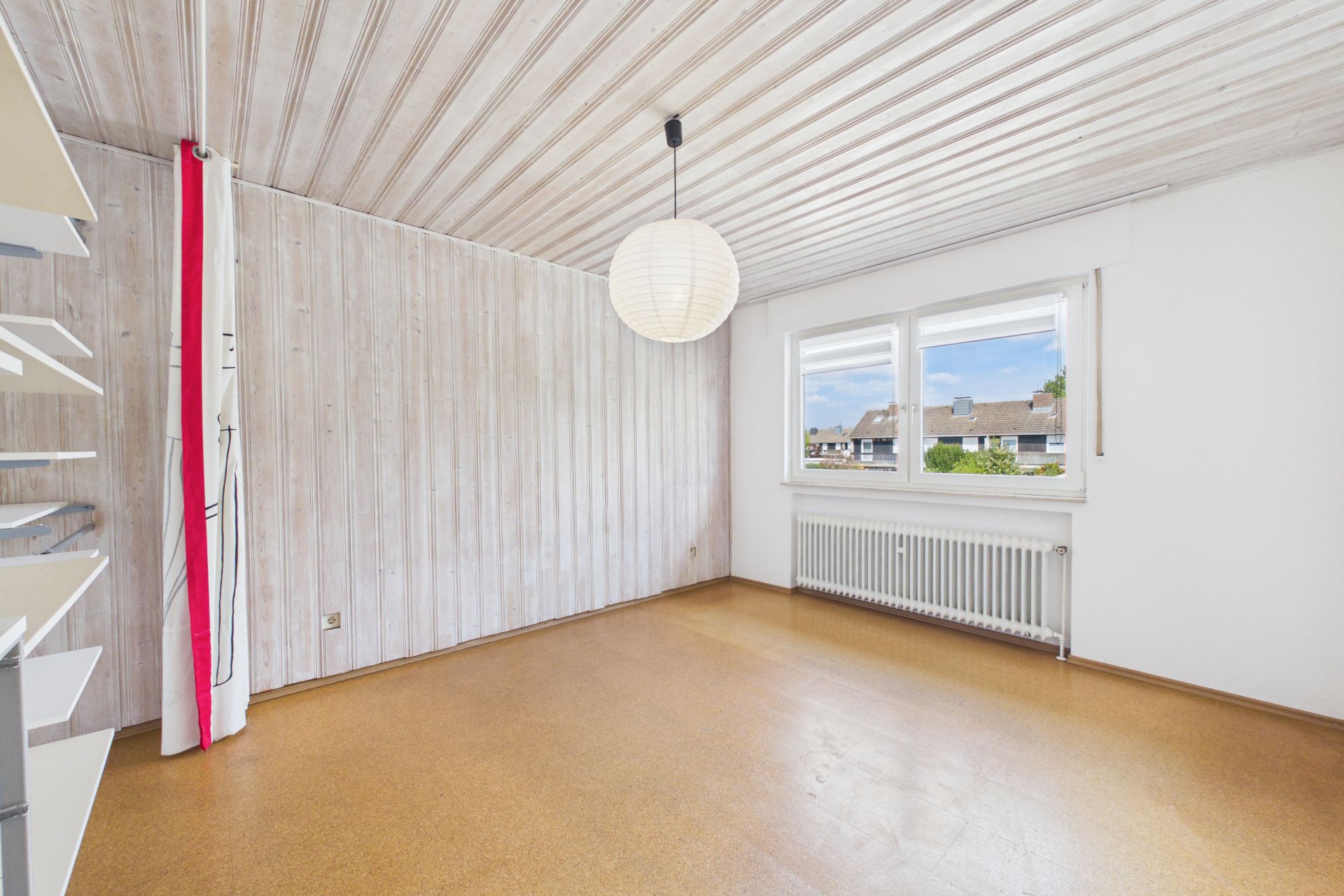 Helles, leeres Zimmer mit Holzdecke, großem Fenster und Heizung unter dem Fenster.