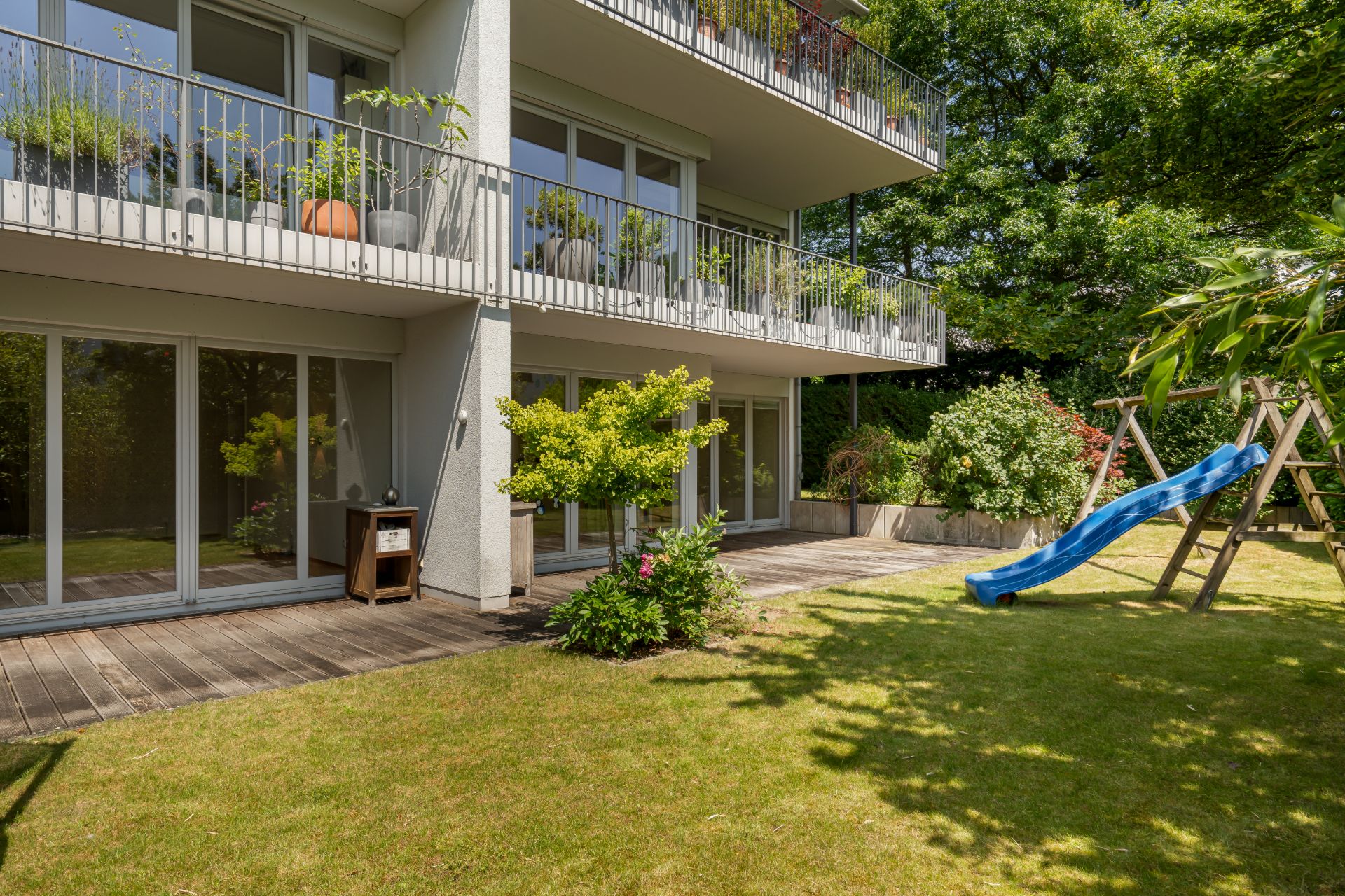 Moderner Balkon und Garten mit Rutsche, Holzboden und vielen Pflanzen.