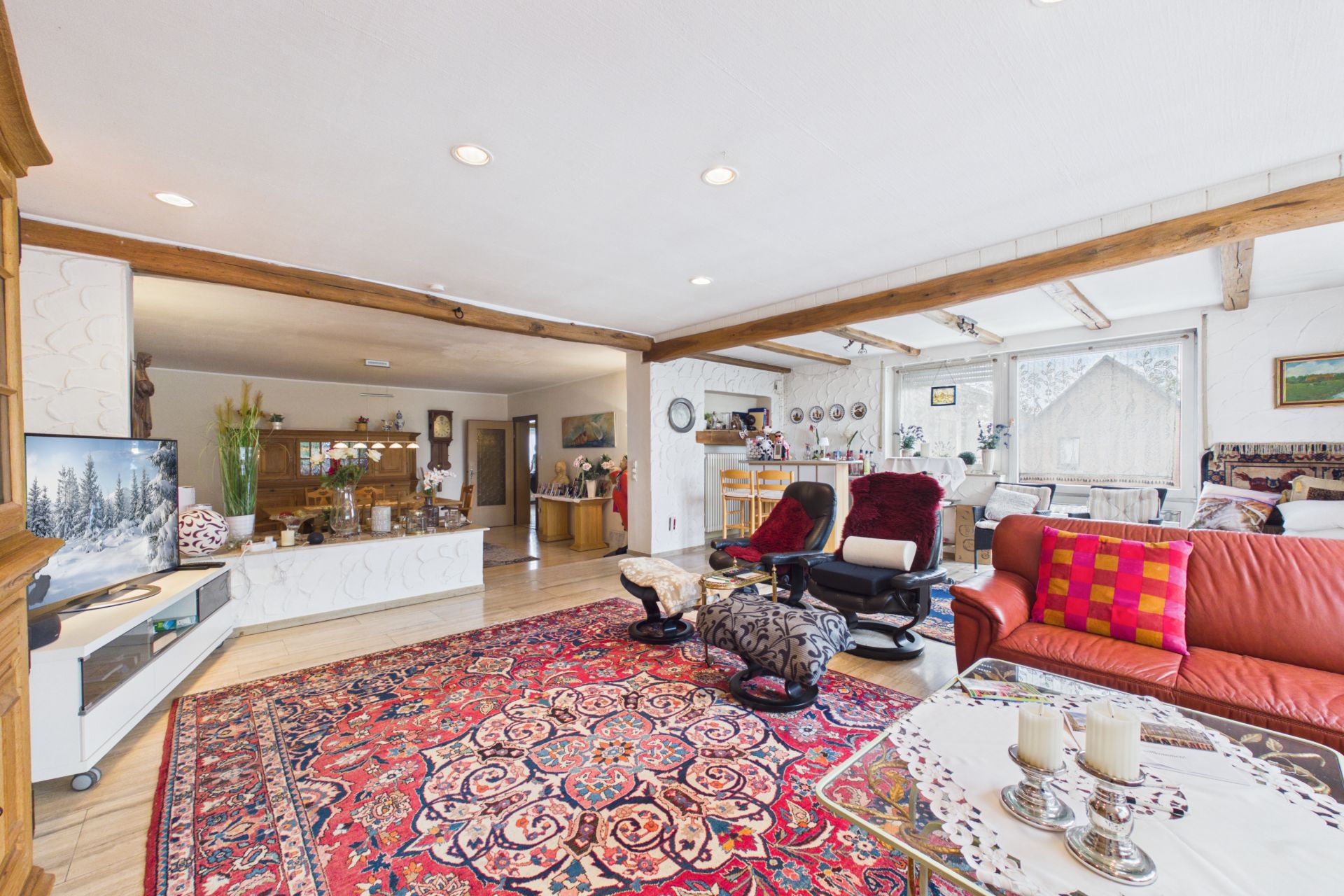 Geräumiges Wohnzimmer mit rotem Teppich, gemütlichen Sesseln, Sofa und großem Fenster.