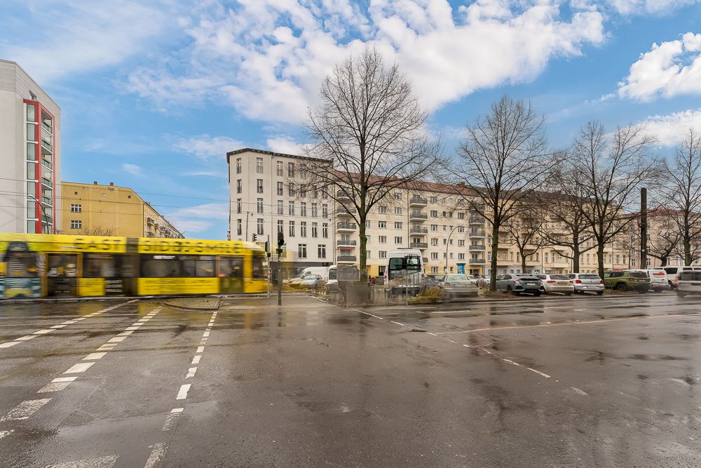 Wohnhäuser an einer Straße mit parkenden Autos, Bäumen und einer gelben Straßenbahn.