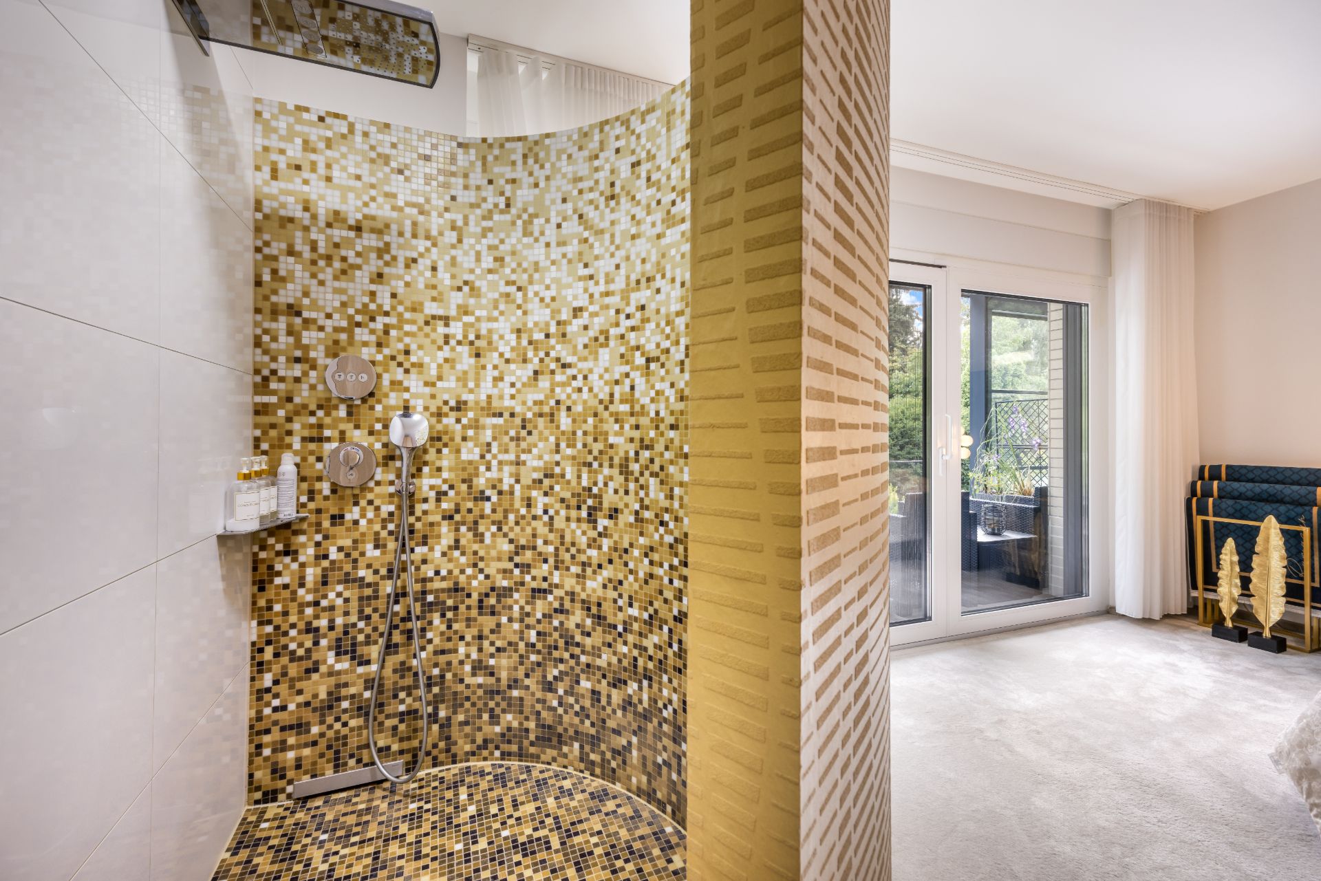 Moderne Dusche mit gold-gelben Mosaikfliesen in einem hellen Wohnraum mit Zugang zur Terrasse.