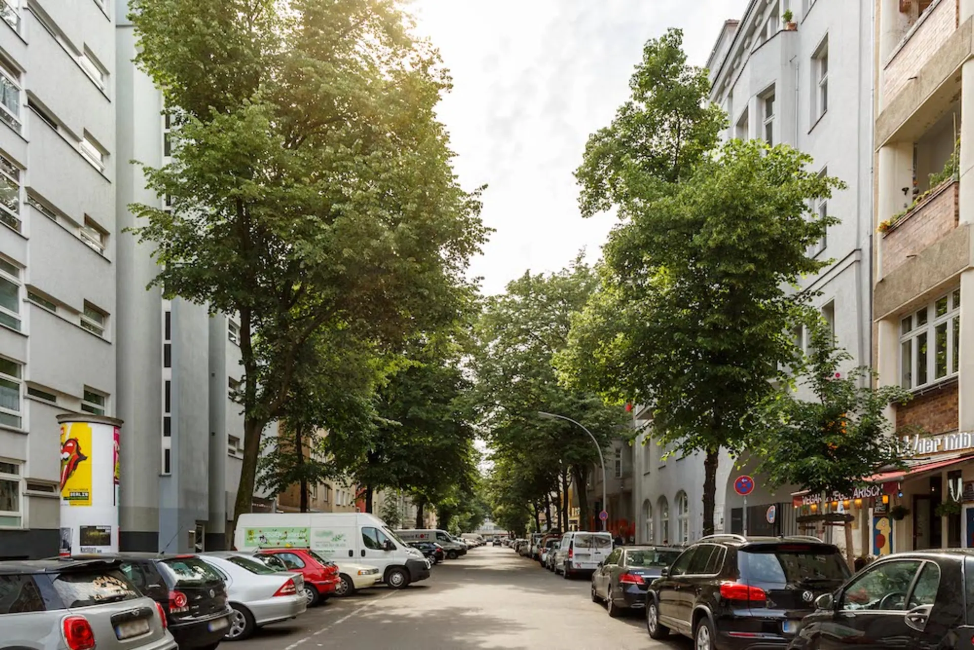 Baumbestandene Wohnstraße mit parkenden Autos und mehrstöckigen Wohnhäusern auf beiden Seiten.