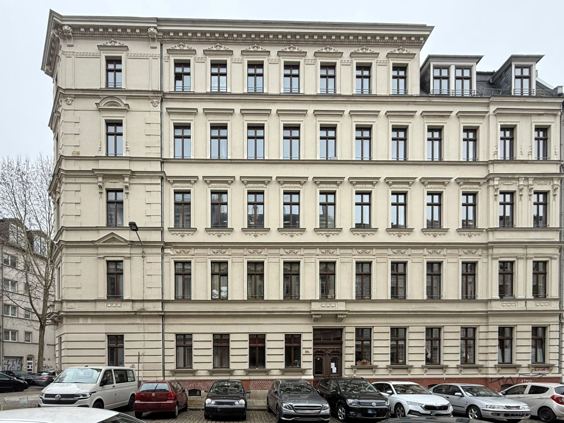 Mehrstöckiges Wohngebäude mit vielen Fenstern und geparkten Autos davor.
