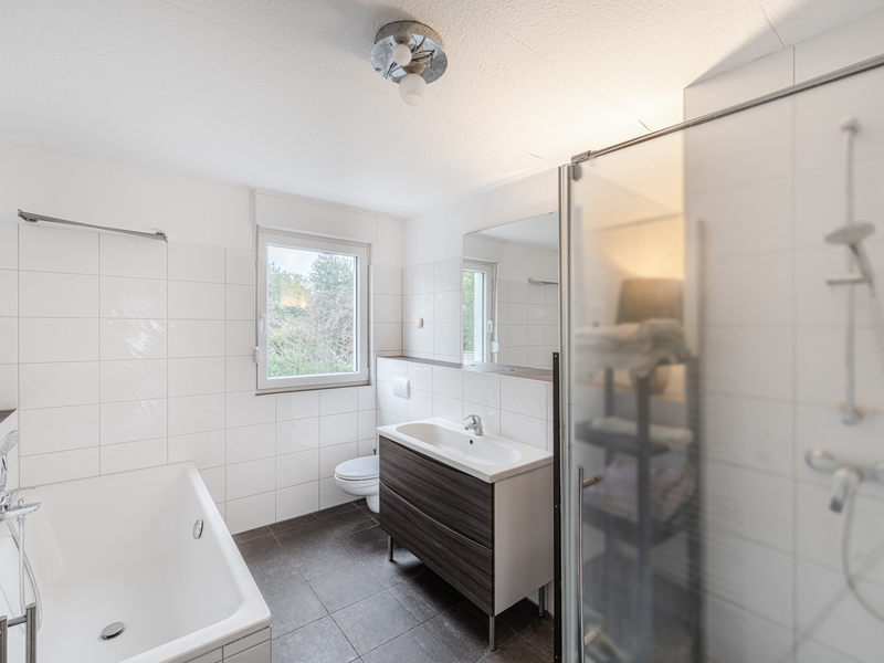 Modernes Badezimmer mit Badewanne, Dusche, Waschbecken, Toilette und Fenster.