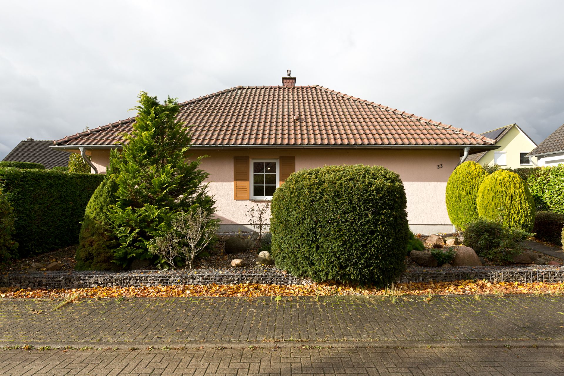 Einfamilienhaus mit rotem Dach, einem Fenster und gepflegtem Vorgarten mit Büschen.