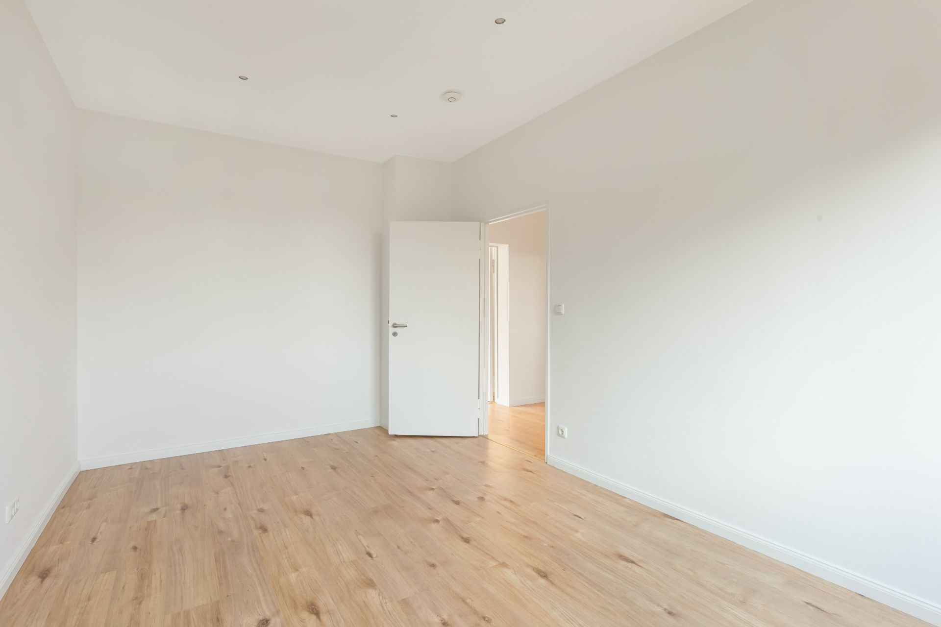 Leerer, heller Raum mit Holzboden und weißer Tür, die halb geöffnet ist.