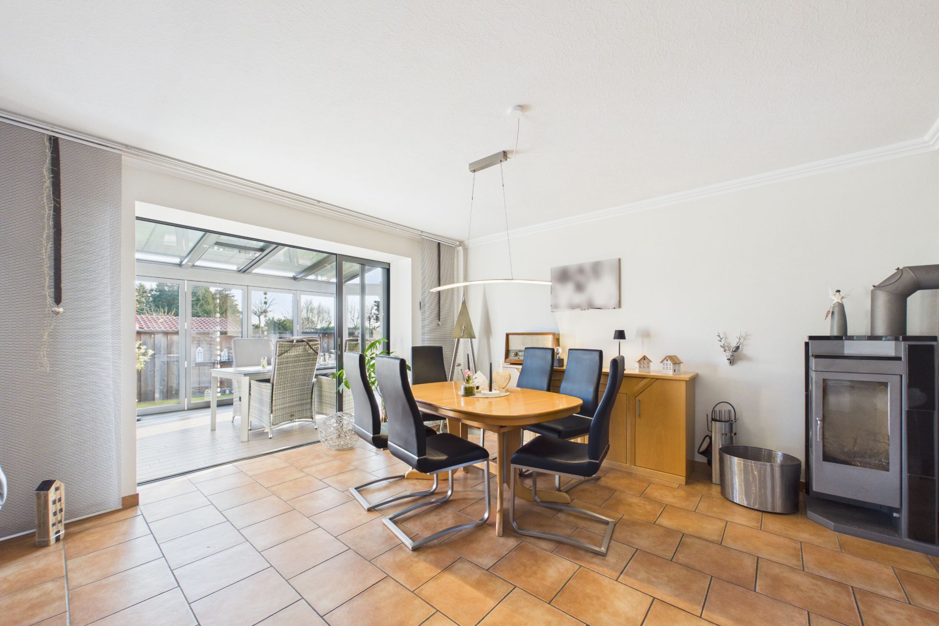 Helles Esszimmer mit rundem Holztisch, schwarzen Stühlen und Zugang zu einer verglasten Terrasse.