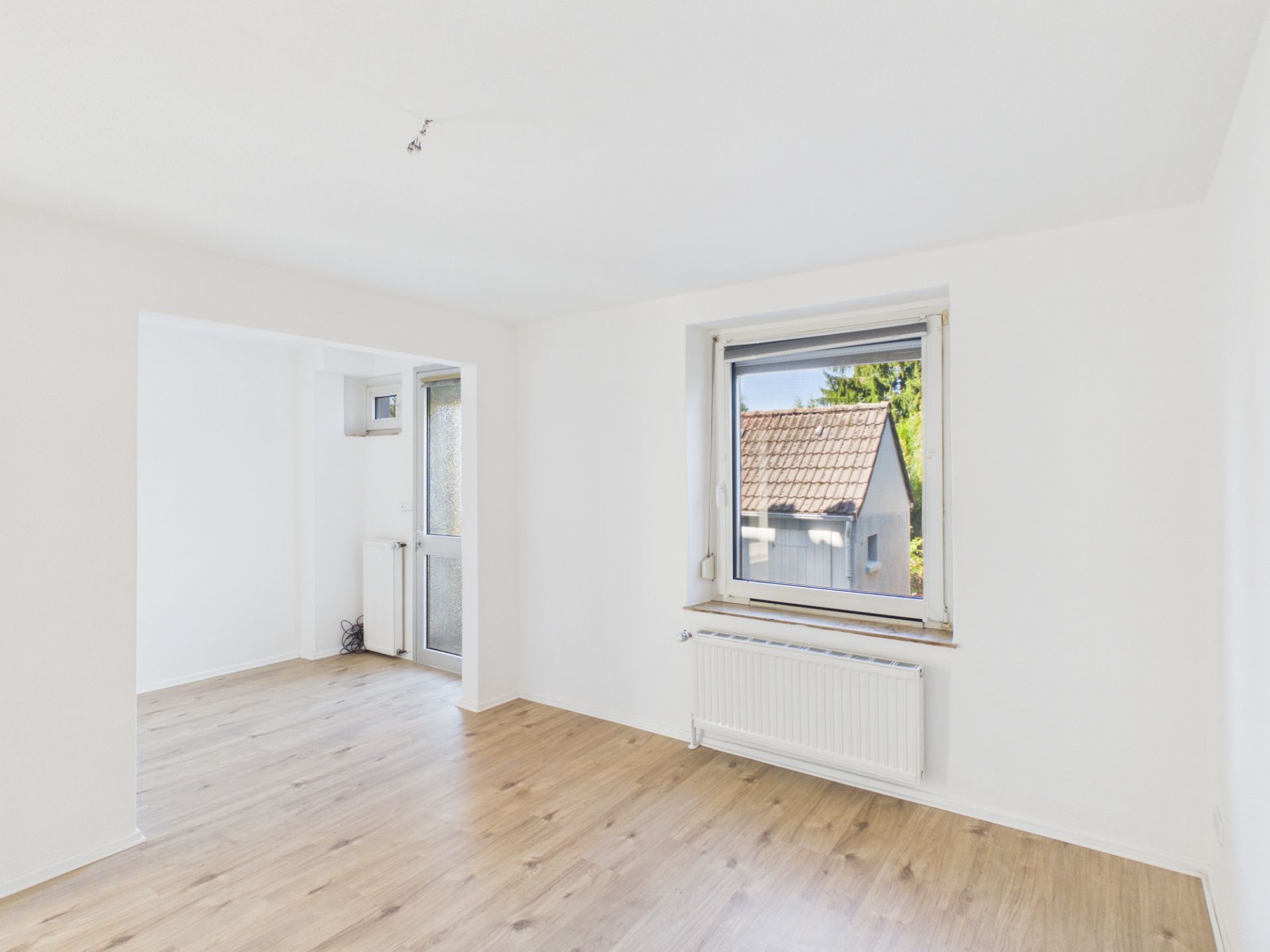 Heller Raum mit Holzboden, Fenster und Tür zum Außenbereich.