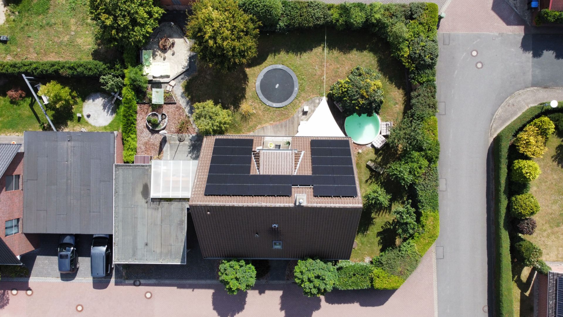 Luftaufnahme eines Hauses mit Solarpaneelen, Garten, Trampolin und kleinem Pool.