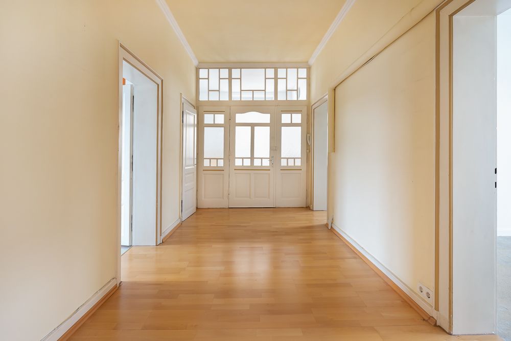 Heller Flur mit Holzboden, mehreren Türen und großen Fenstern am Ende.