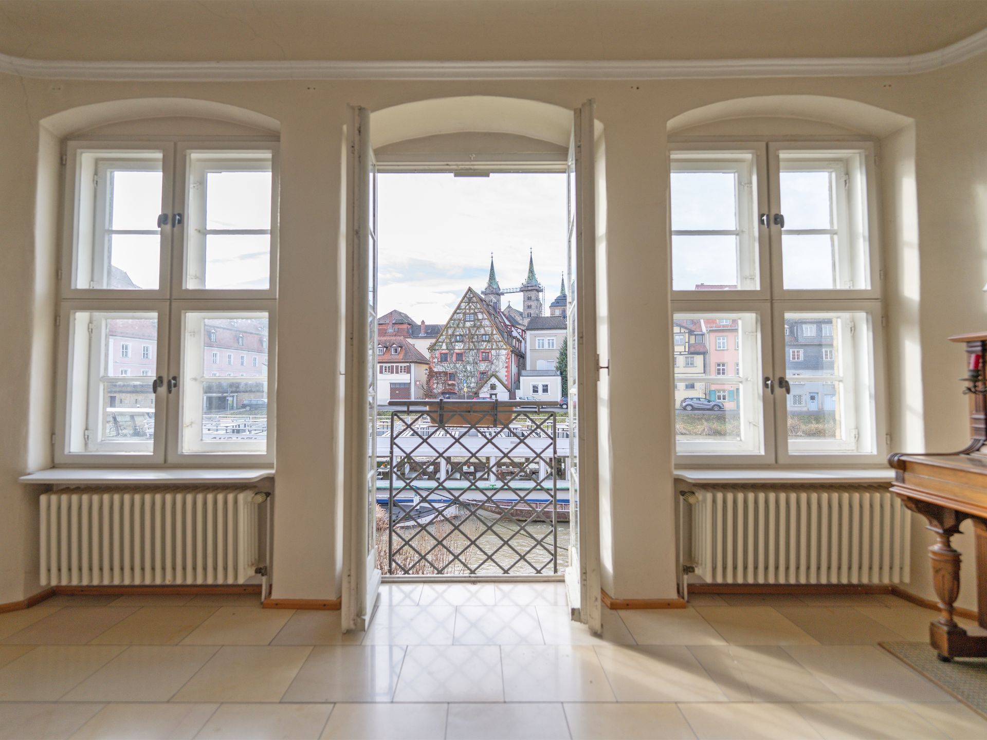 Helles Zimmer mit drei Fenstern und Balkonblick auf Altstadthäuser.