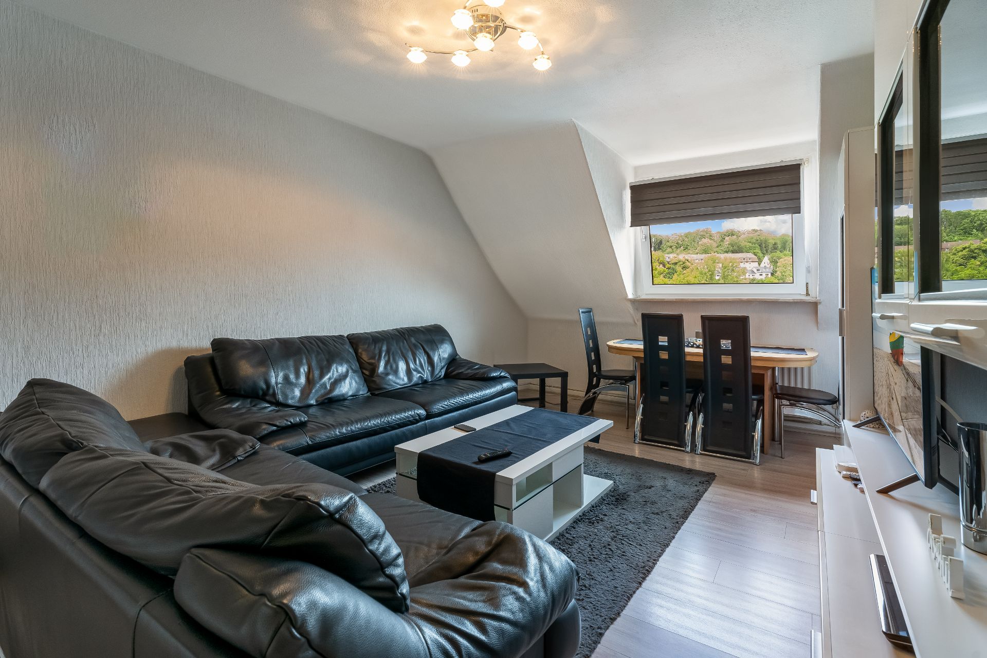 Wohnzimmer mit zwei schwarzen Ledersofas, Couchtisch, Esstisch und großem Fenster.