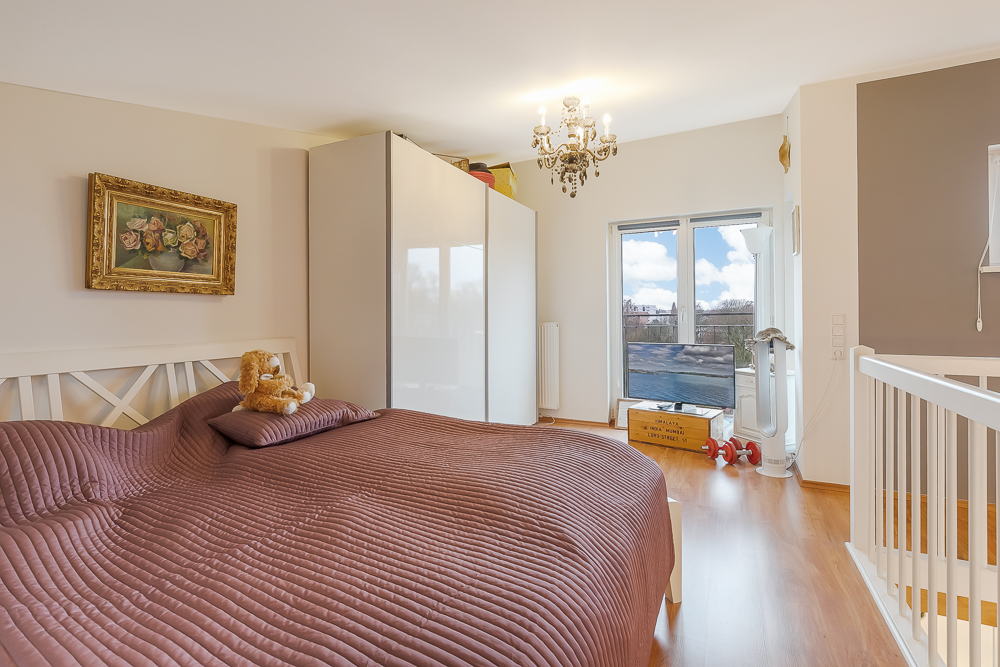 Schlafzimmer mit großem Bett, Kuscheltier, Kleiderschrank, Kronleuchter und großem Fenster.