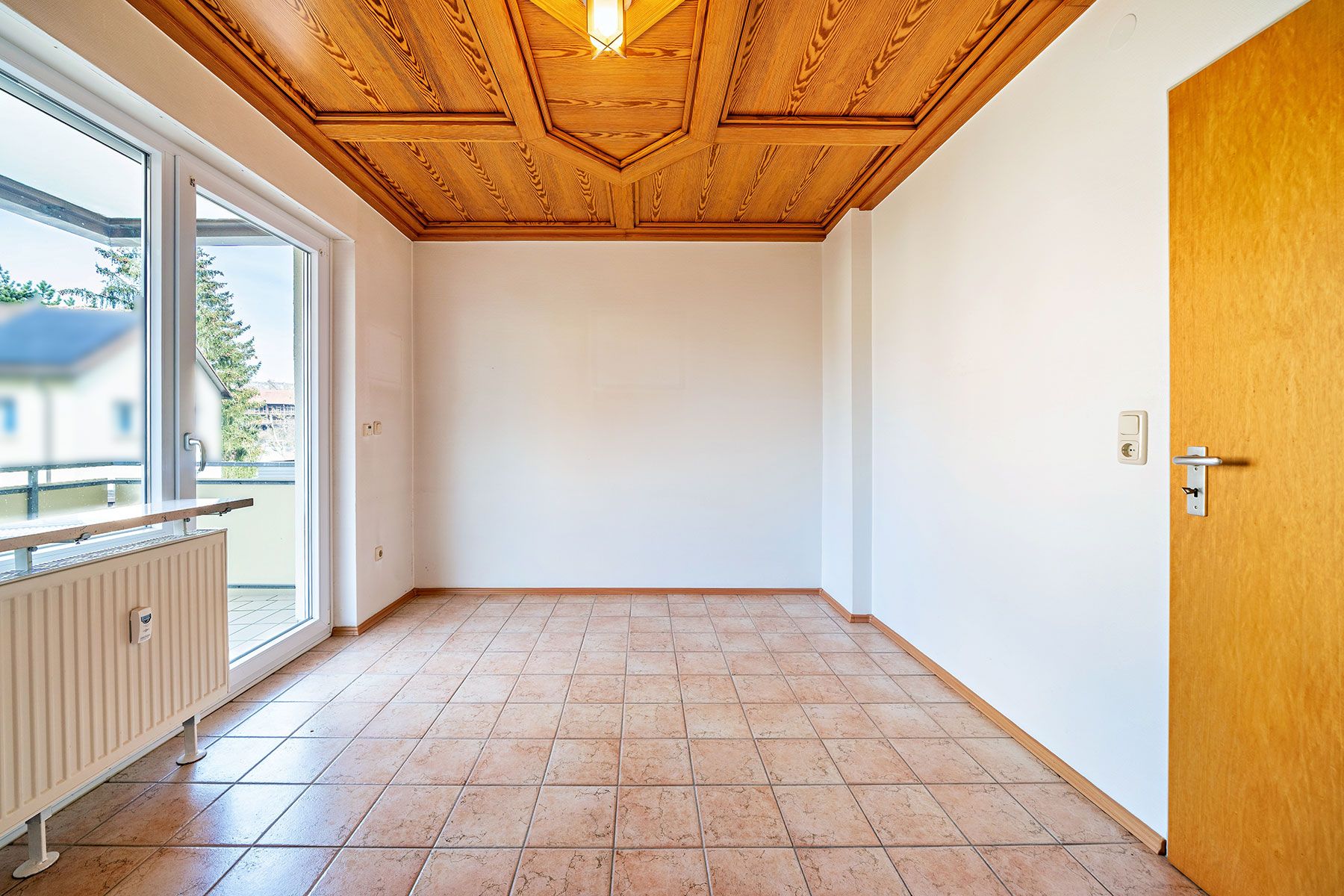 Leerer Raum mit Fliesenboden, Holzdecke, Tür und Fenster mit Zugang zu einem Balkon.