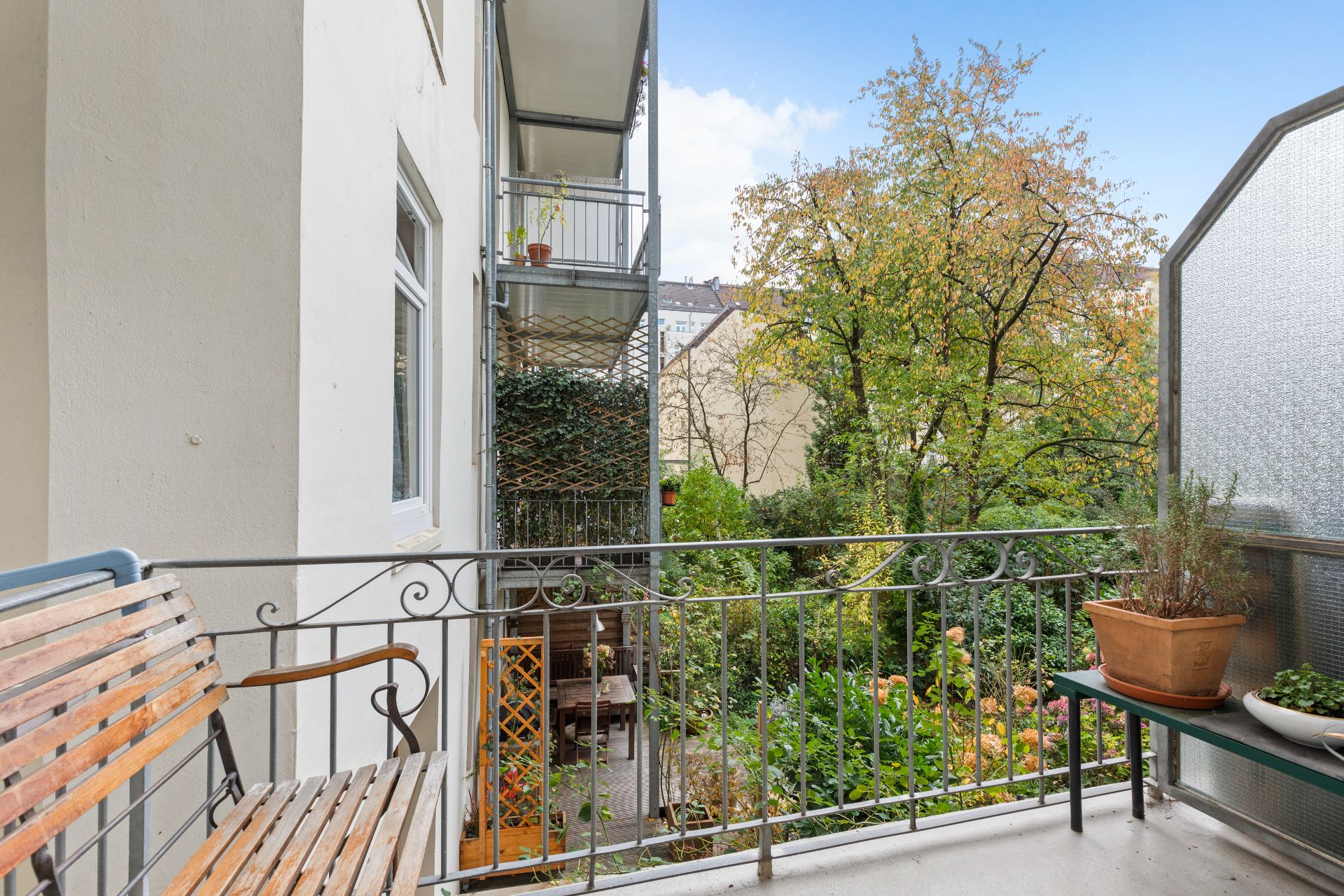 Balkon mit Holzbank, Pflanzen und Blick auf einen grünen Garten mit Bäumen.