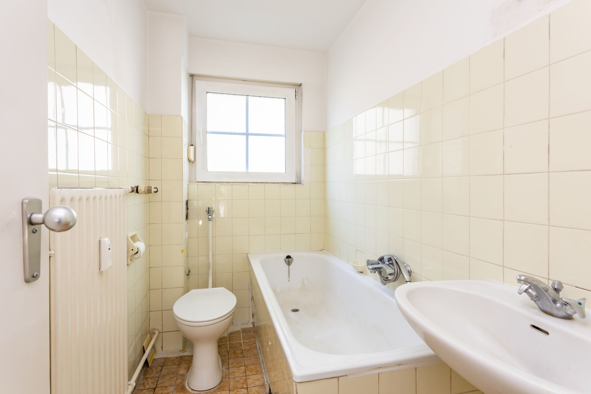 Kleines Badezimmer mit Badewanne, Waschbecken, Toilette und Fenster.