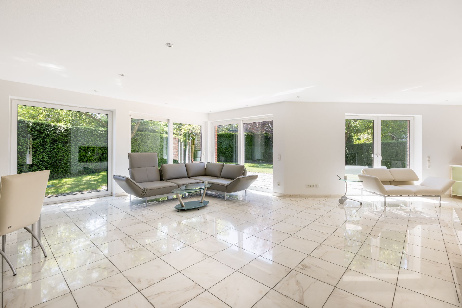 Helles Wohnzimmer mit Ecksofa, Marmorboden und großen Fenstern zum Garten.