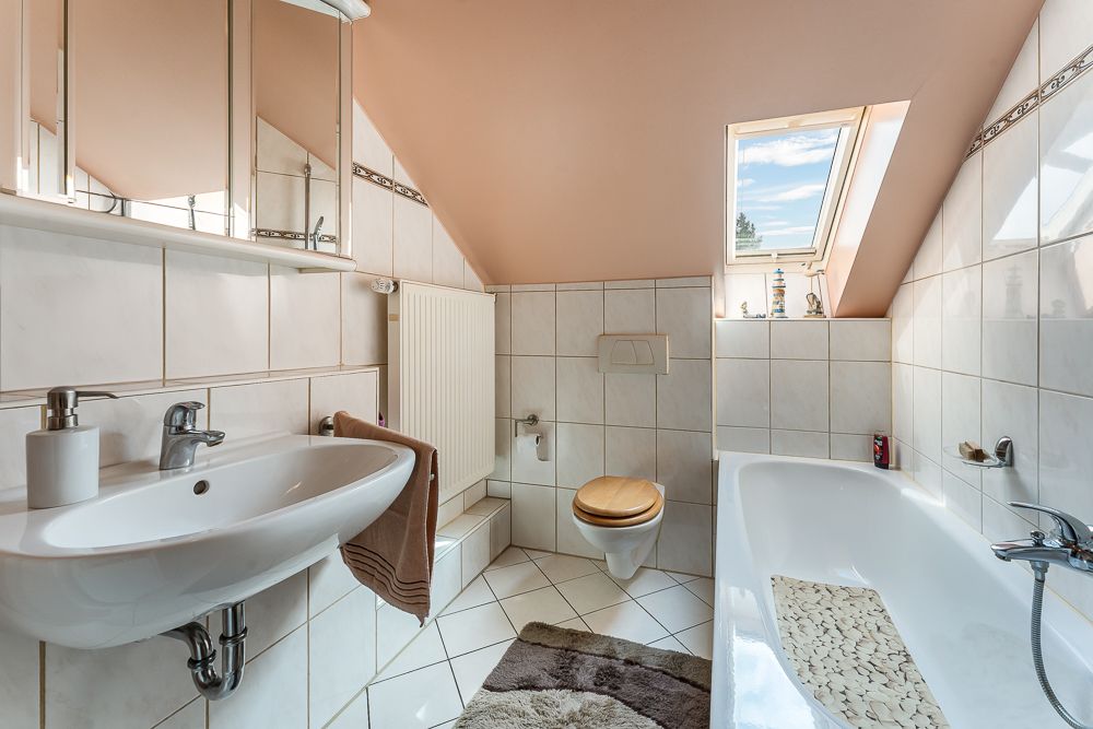 Modernes Badezimmer mit Waschbecken, Badewanne, Toilette, Spiegeln und Dachfenster.
