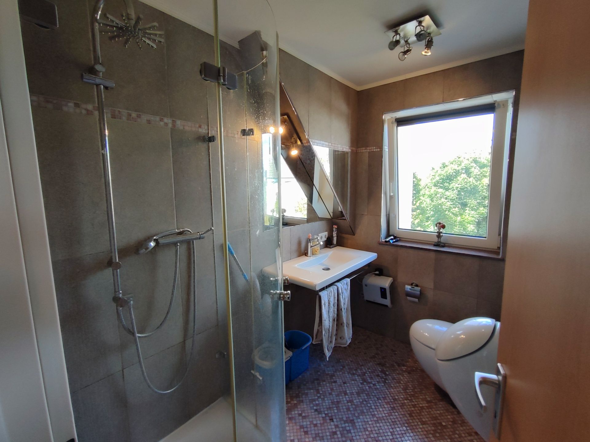 Modernes Badezimmer mit Dusche, Waschbecken, WC und großem Fenster.