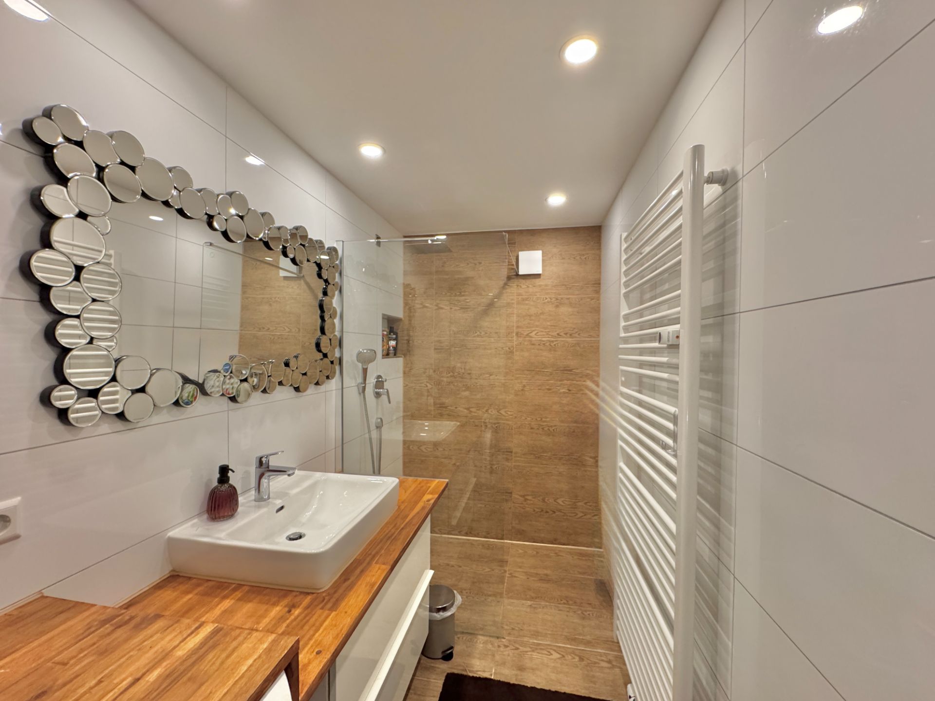 Modernes Badezimmer mit Holzwaschtisch, rundem Spiegel und ebenerdiger Dusche.
