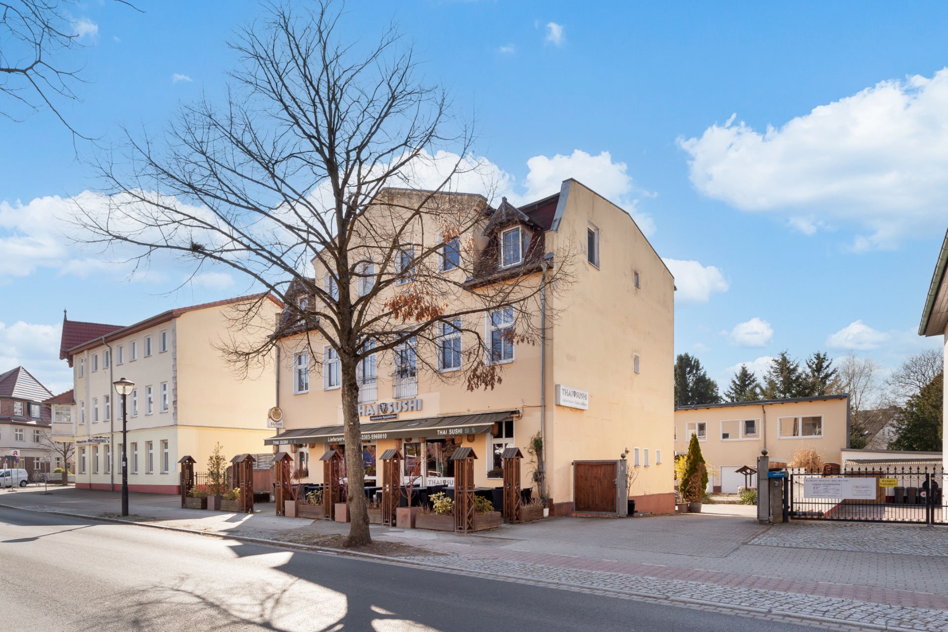 Wohnhaus mit Terrasse an einer Straße, im Vordergrund steht ein Baum ohne Blätter.