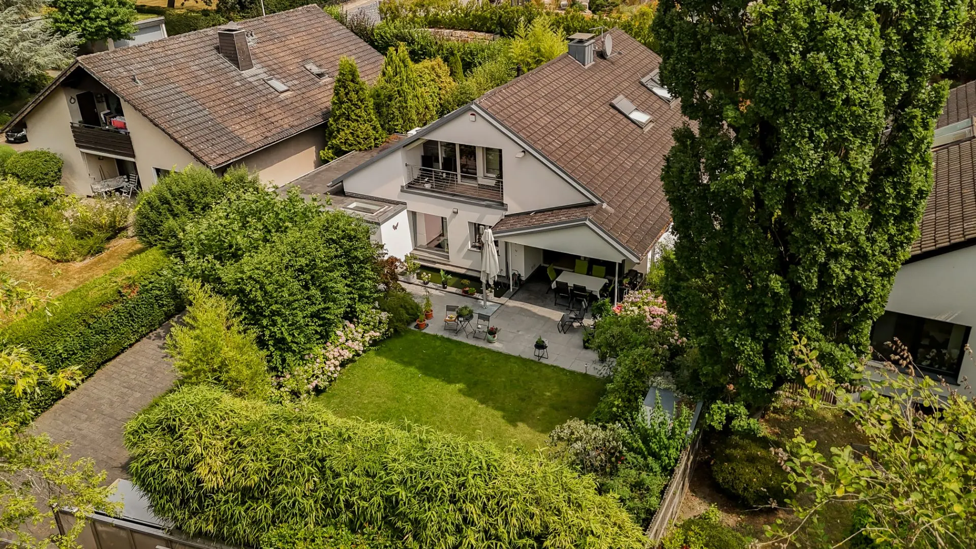 Luftaufnahme eines Einfamilienhauses mit Garten, Terrasse und umliegender Bepflanzung.