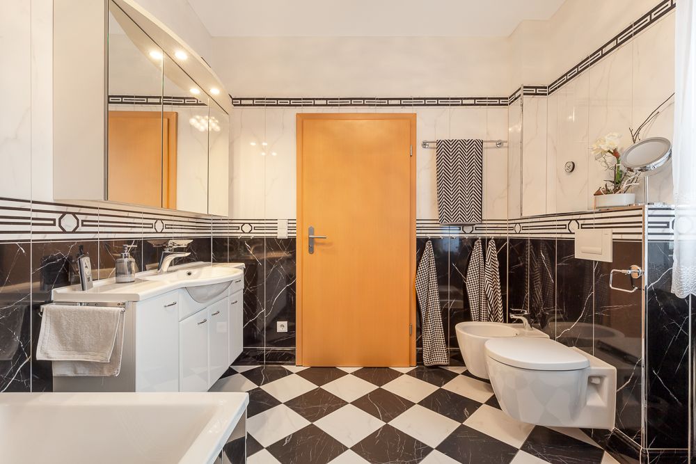Modernes Badezimmer mit schwarz-weiß karierten Fliesen, Waschbecken, WC, Bidet und Holz­tür.