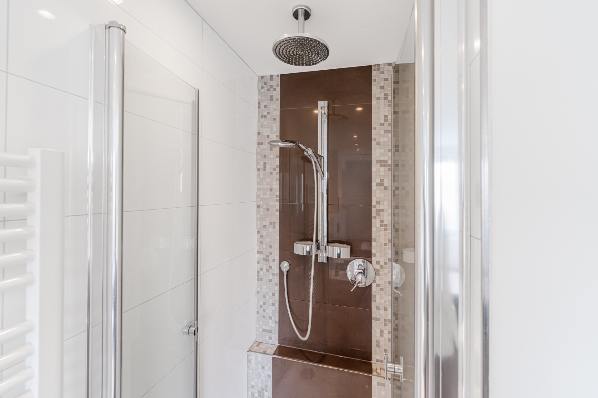 Moderne Dusche mit Glastüren und Regenduschkopf, braun-weiße Fliesen an der Wand.