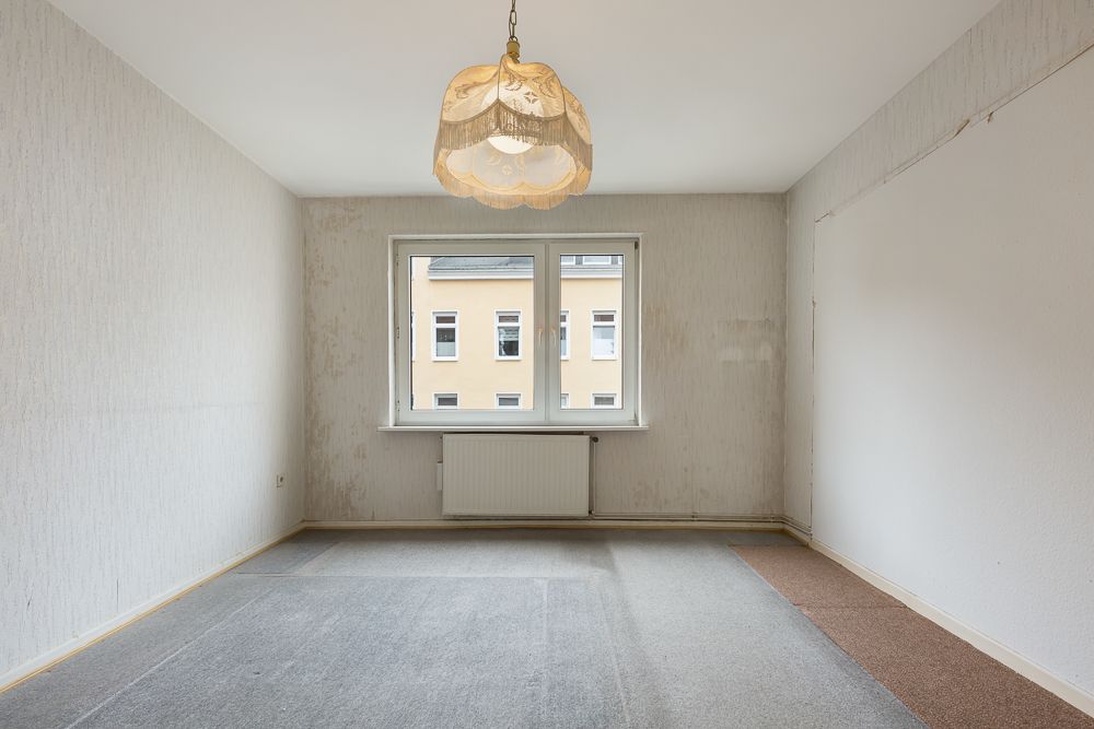 Leerer Raum mit Teppichboden, Fenster, Heizung und Deckenlampe.