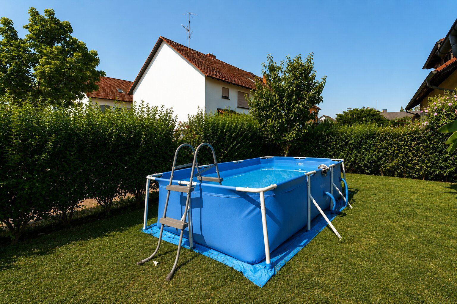 Ein rechteckiger Aufstellpool mit Leiter steht im Garten auf einer grünen Rasenfläche.