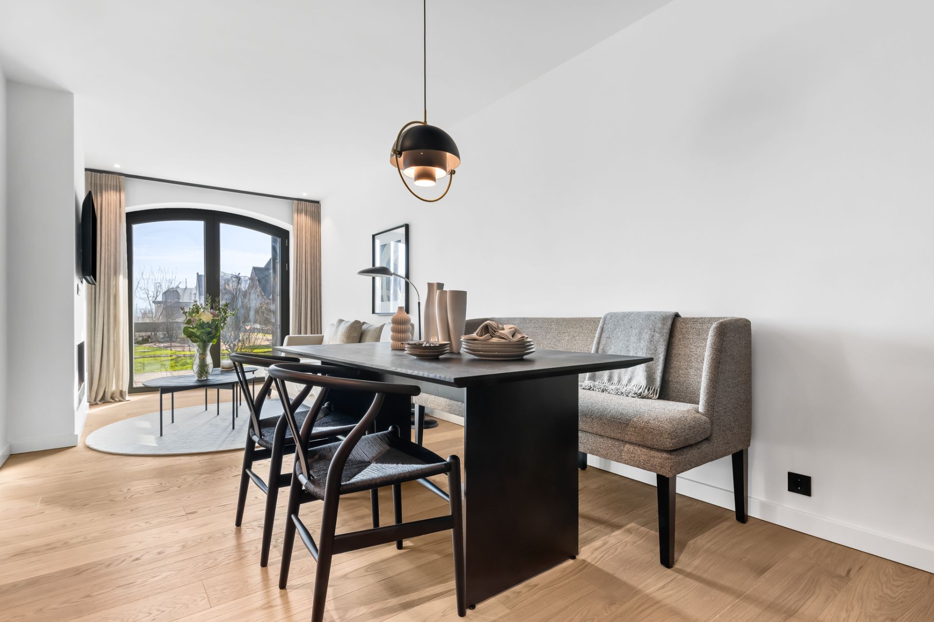 Heller Essbereich mit schwarzem Tisch, Stühlen, Sofa und großer Fensterfront im Hintergrund.