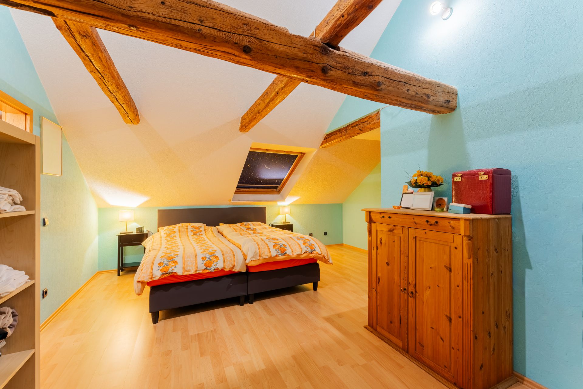 Helles Schlafzimmer im Dachgeschoss mit Holzbalken, Doppelbett und Kommode.