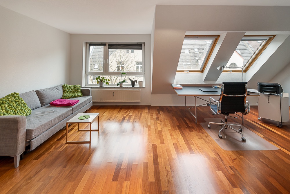 Helles Zimmer mit Sofa, Couchtisch, Schreibtisch und zwei großen Dachfenstern.