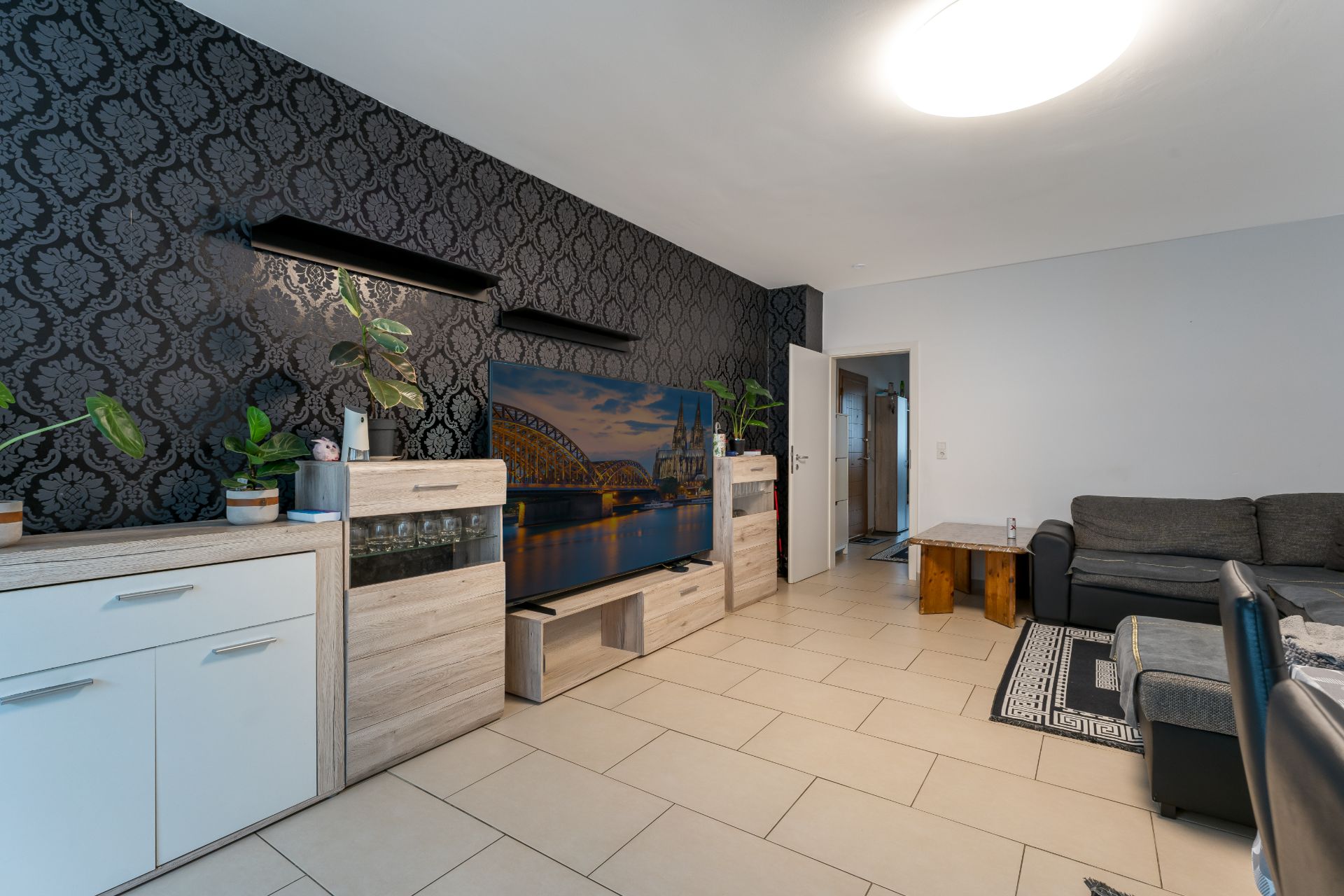 Wohnzimmer mit dunkler Tapete, Fernseher, grauem Sofa und Holzmöbeln.