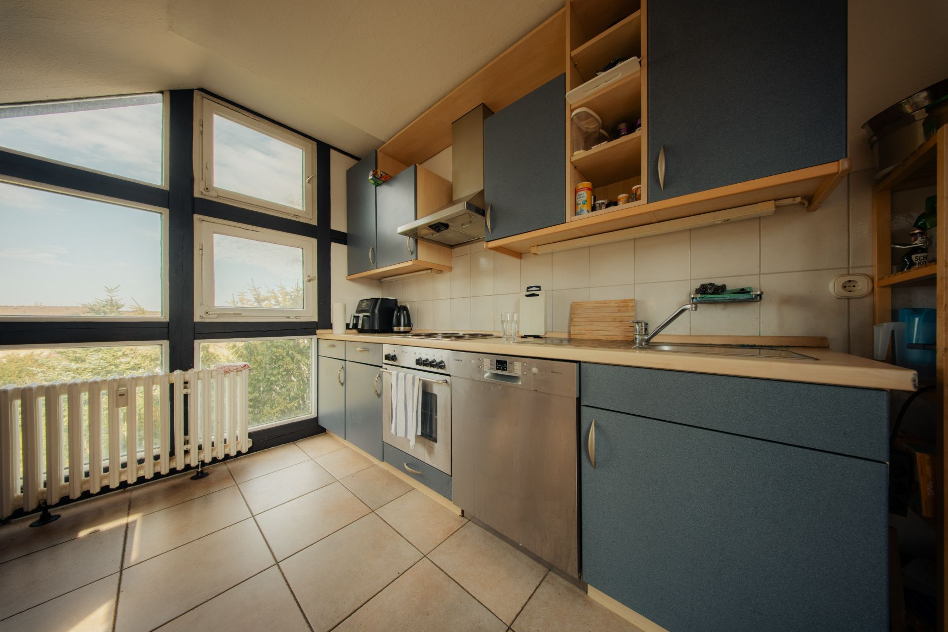 Moderne Küche mit blauen Schränken, großen Fenstern und Fliesenboden.