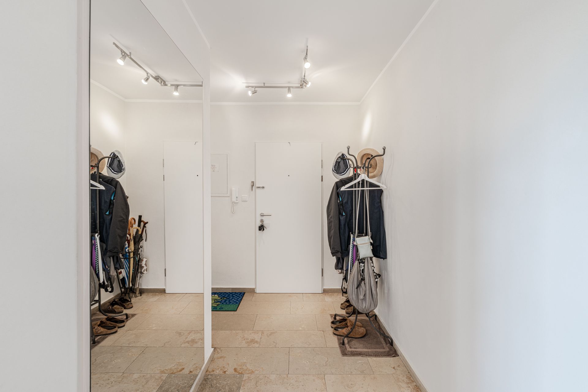 Geräumiger Flur mit Garderobenständern, Jacken, Schuhen und Spiegel an der Wand.