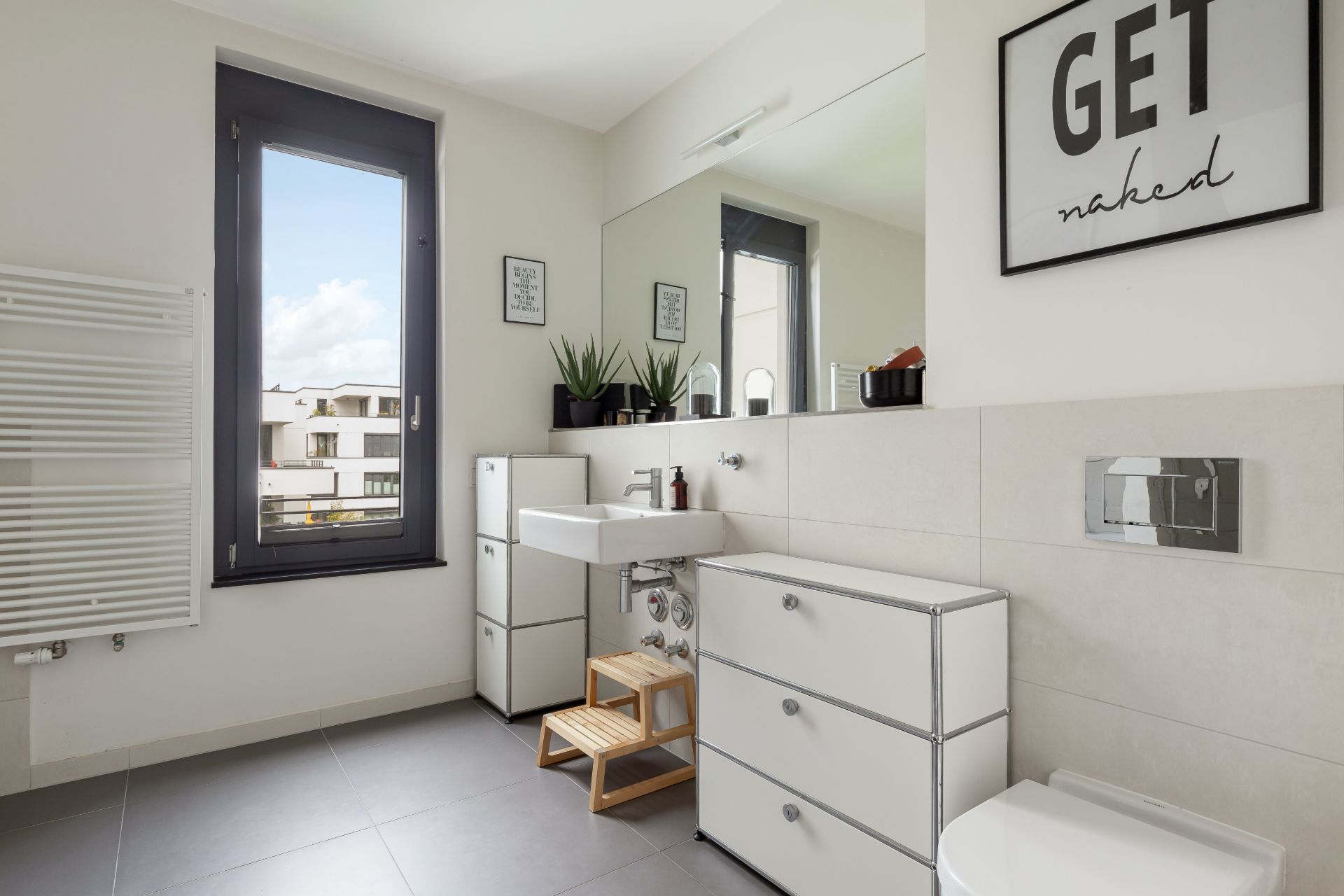 Modernes Badezimmer mit Fenster, Waschbecken, Spiegel, Schränken und Toilette.