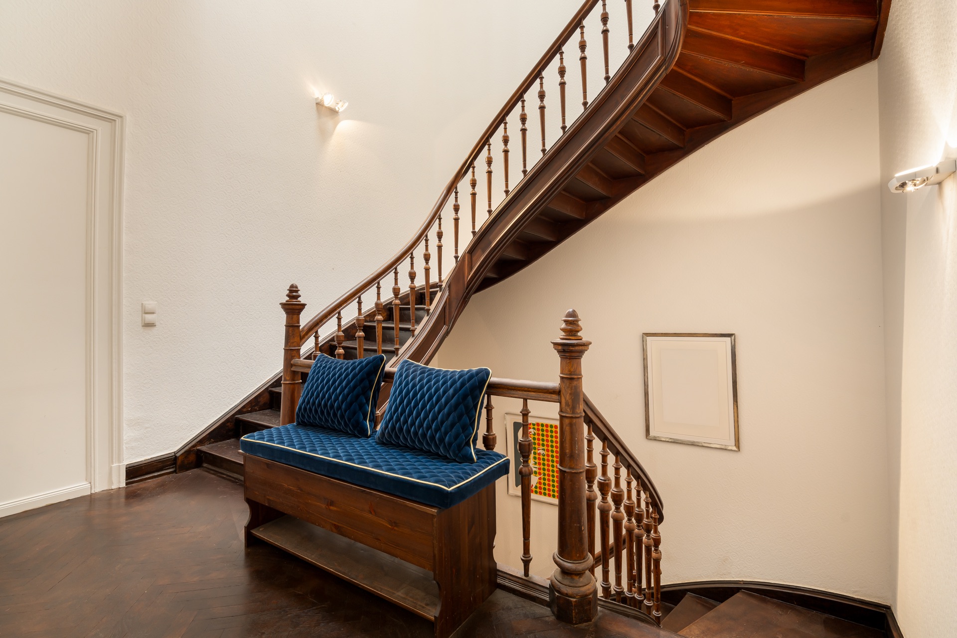 Holztreppe mit blauer Sitzbank und Kissen in einem hellen Flur mit weißer Wand.