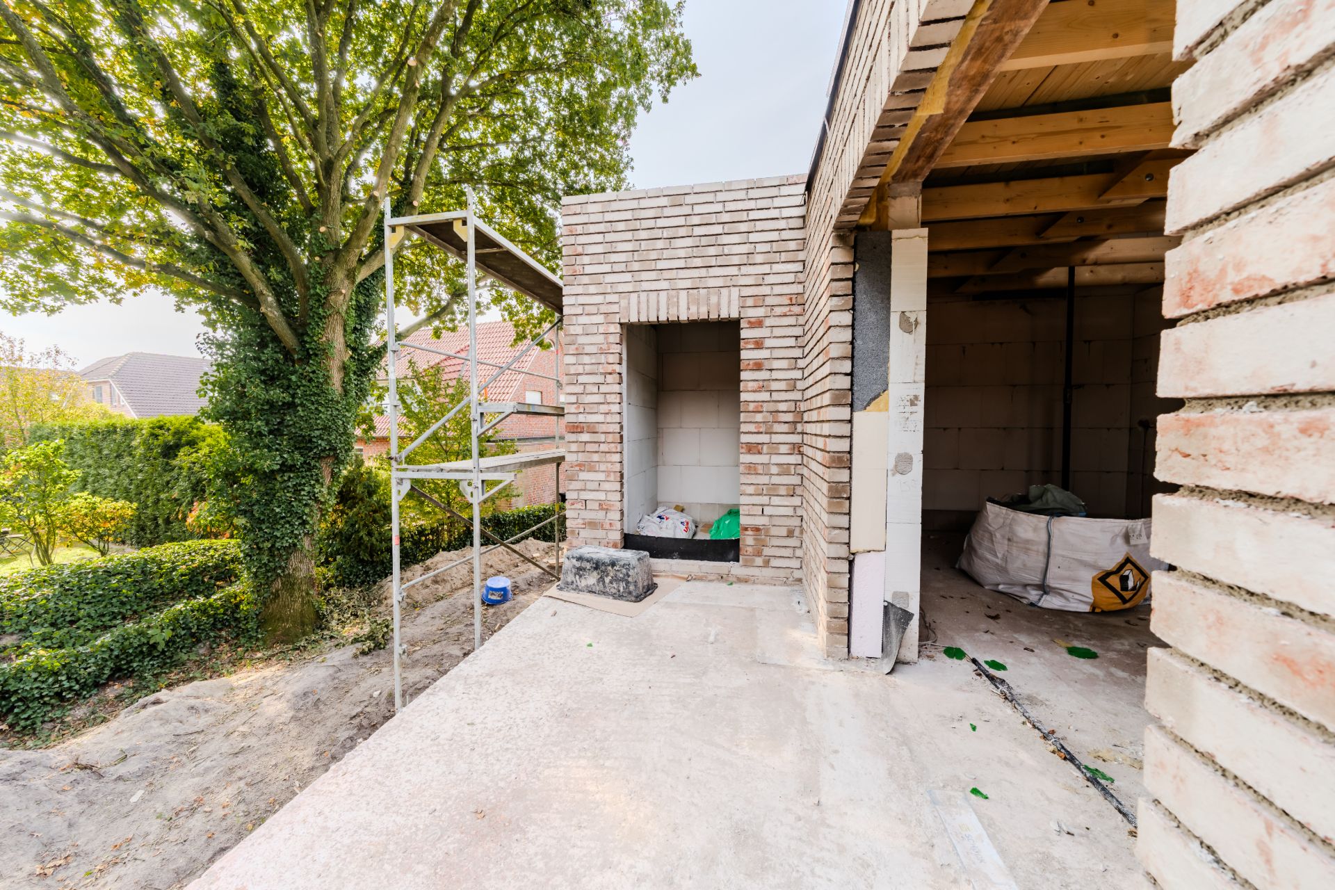 Haus im Bau mit Backsteinmauern und Gerüst neben einem großen Baum im Garten.