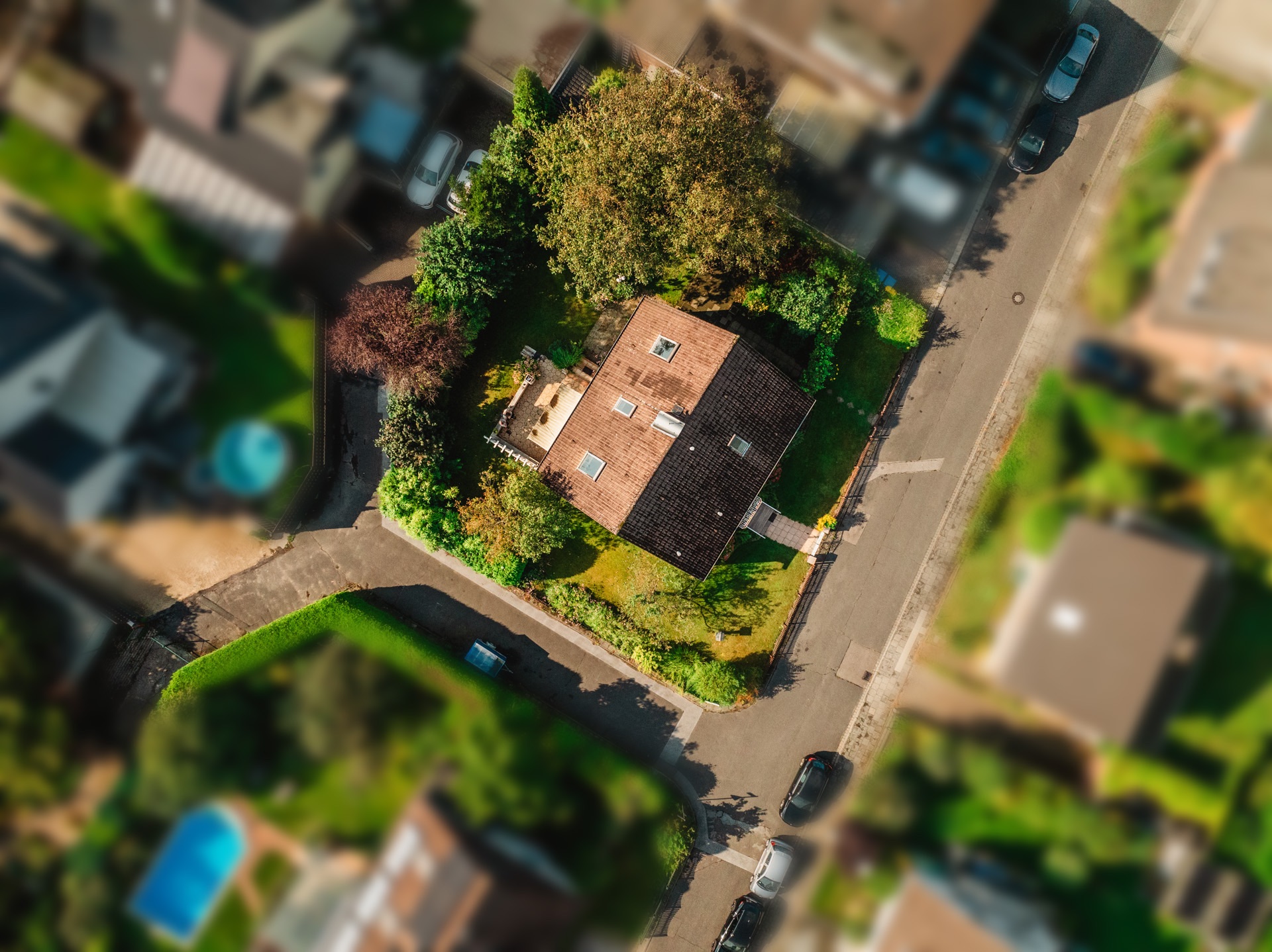 Luftaufnahme eines Einfamilienhauses mit Garten und Bäumen an einer ruhigen Straße.
