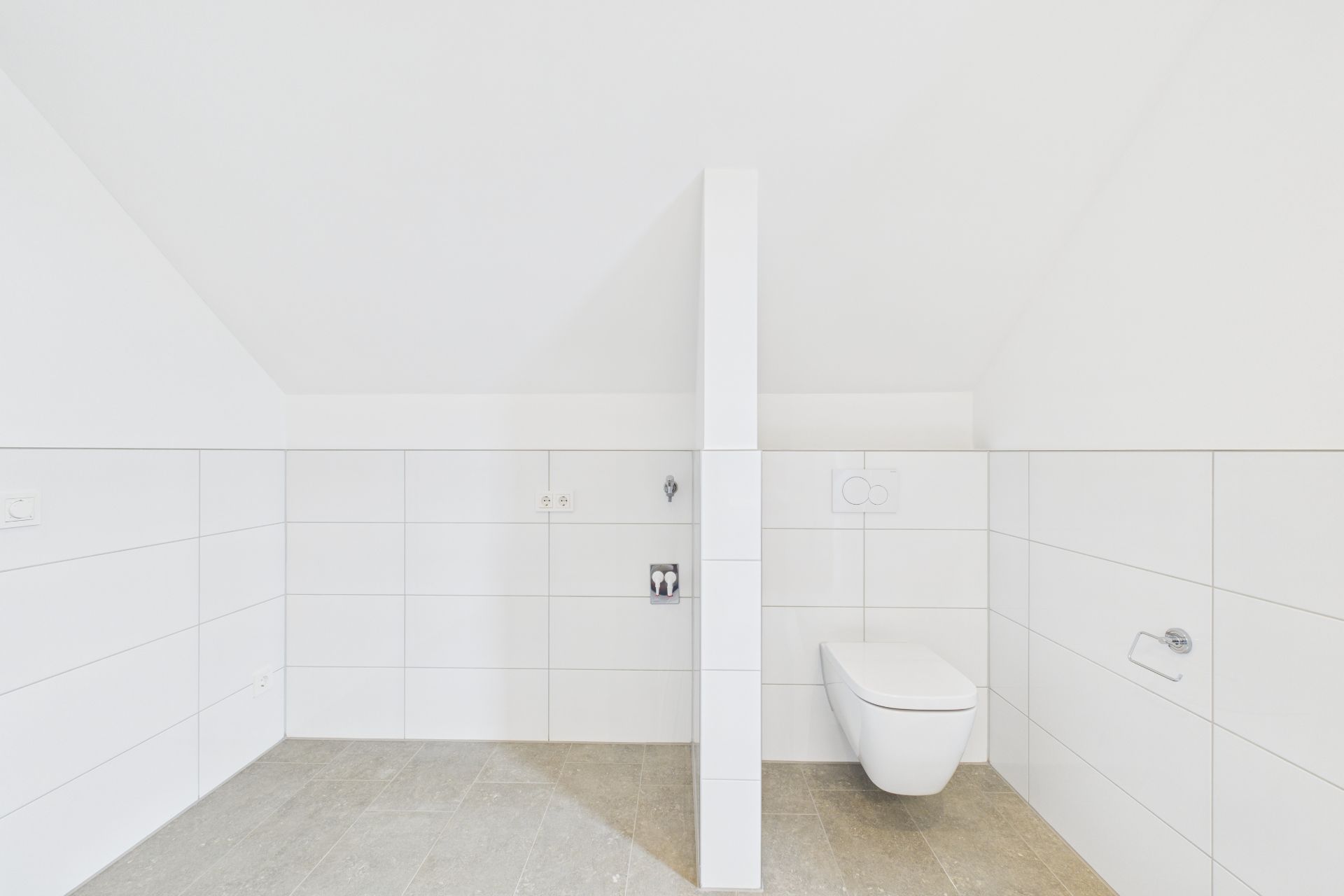 Modernes, weiß gefliestes Badezimmer mit wandhängender Toilette und Trennwand.