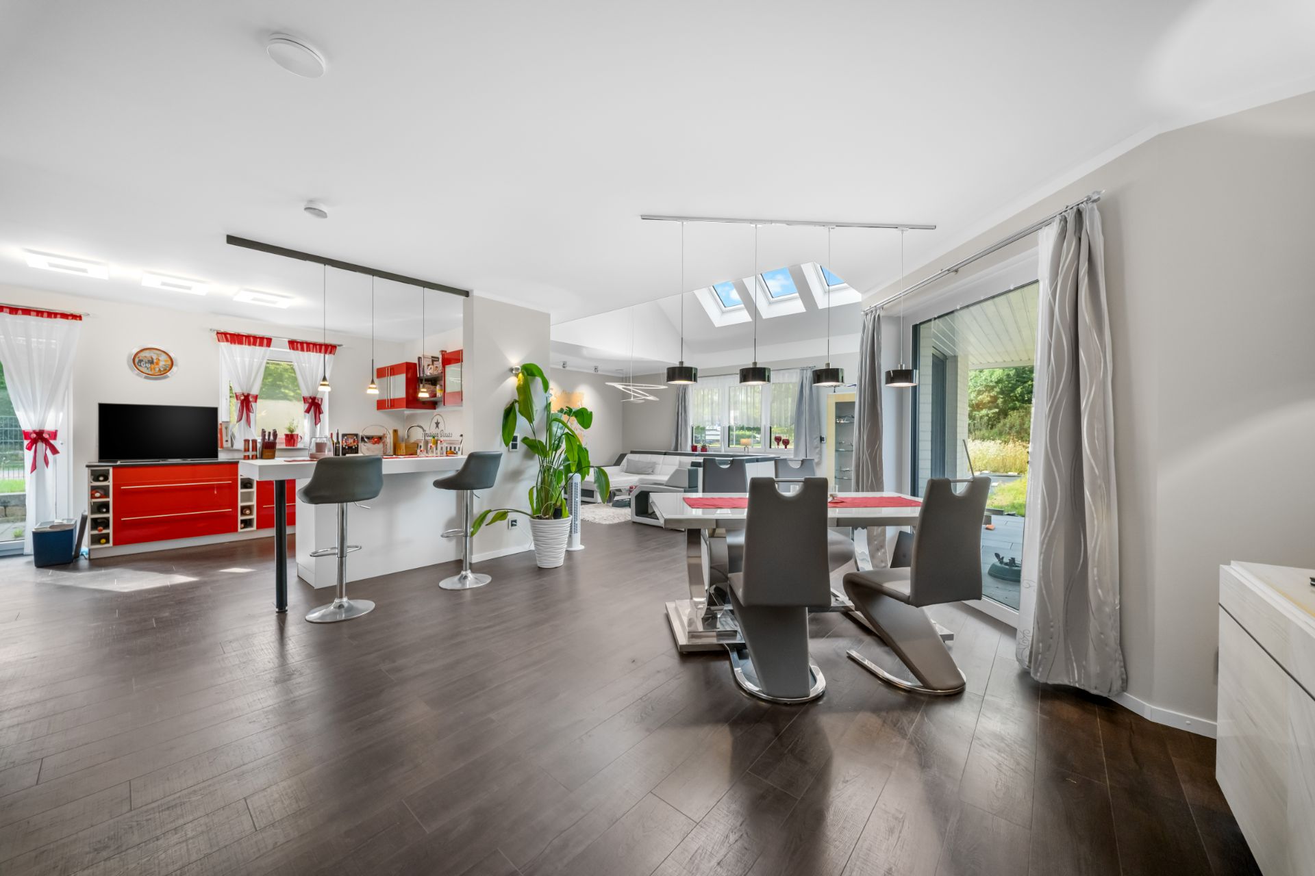 Helles Wohn- und Esszimmer mit großen Fenstern, moderner Küche und dunklem Holzboden.